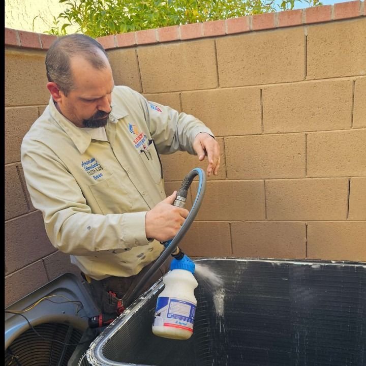 HVAC technician cleans an AC unit's coils outdoors with a bottle and hose.