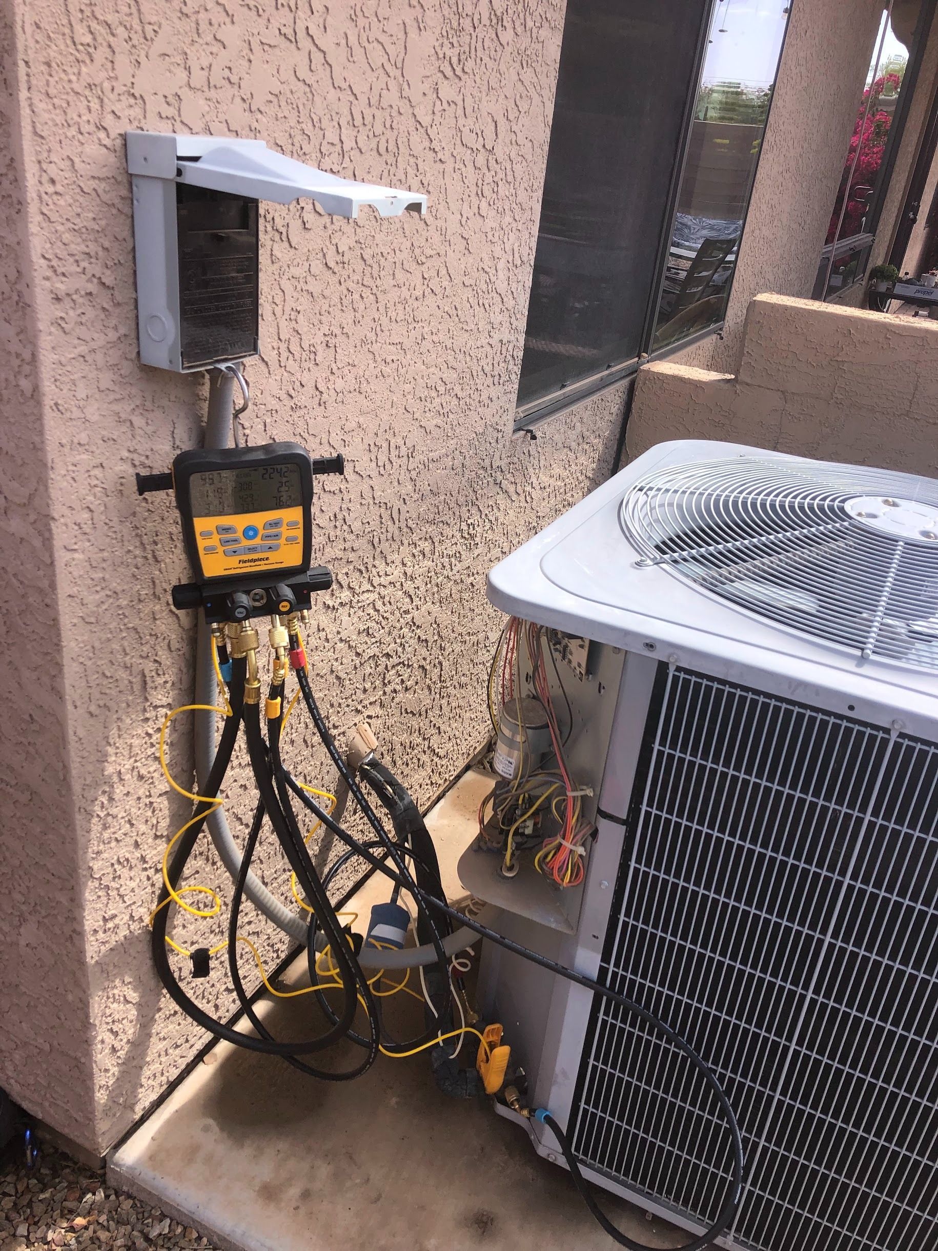 HVAC technician testing air conditioner unit with gauges and hoses attached to a wall-mounted box.