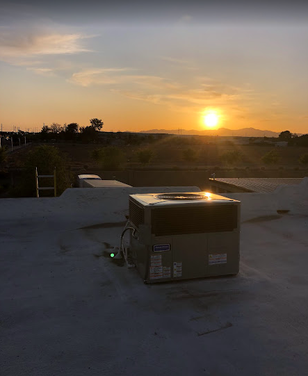 Air conditioning unit on a flat roof at sunset. Orange sun over a distant mountain range.