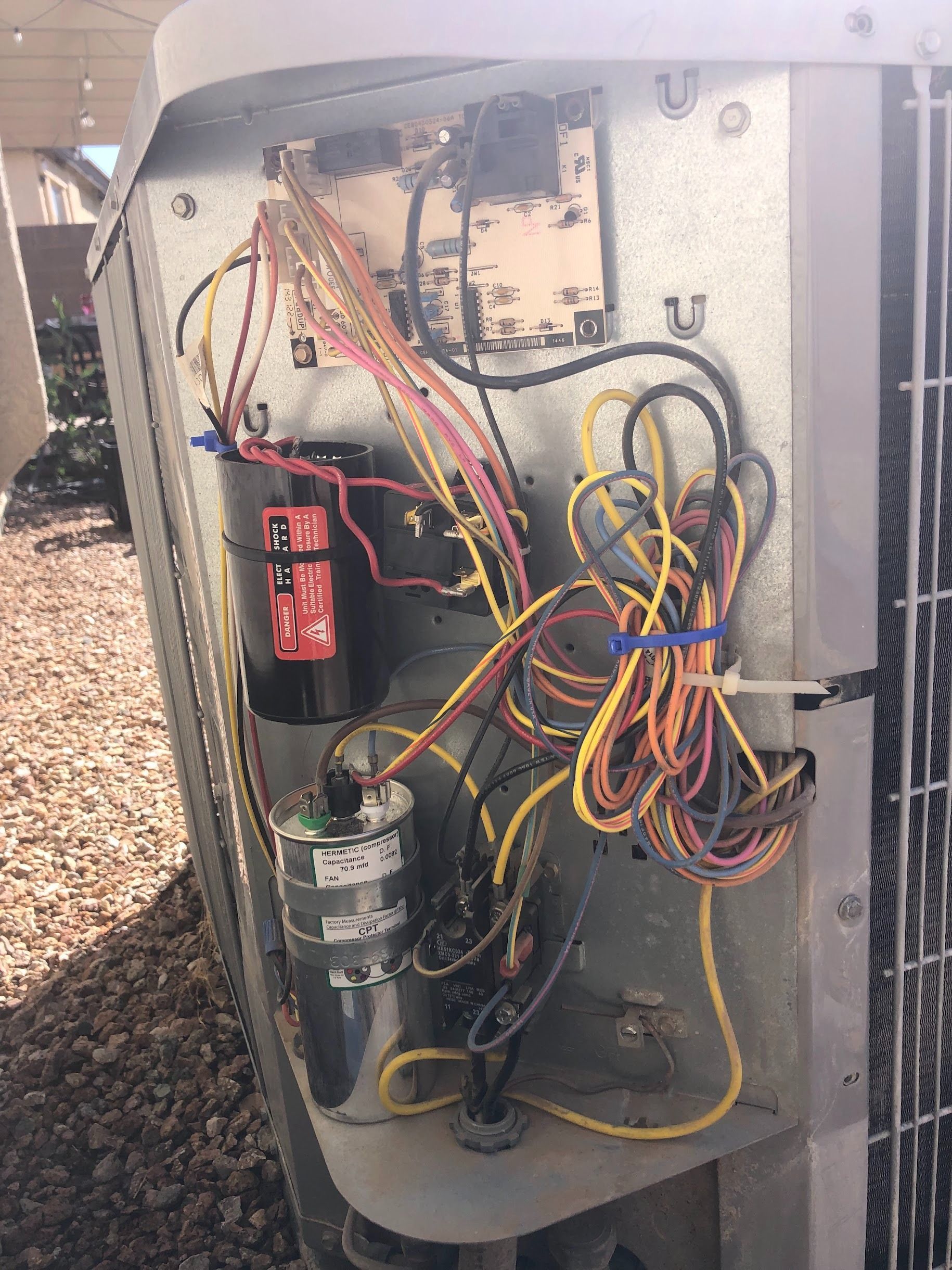 Open view of an air conditioner's electrical components; wires and capacitors of various colors.