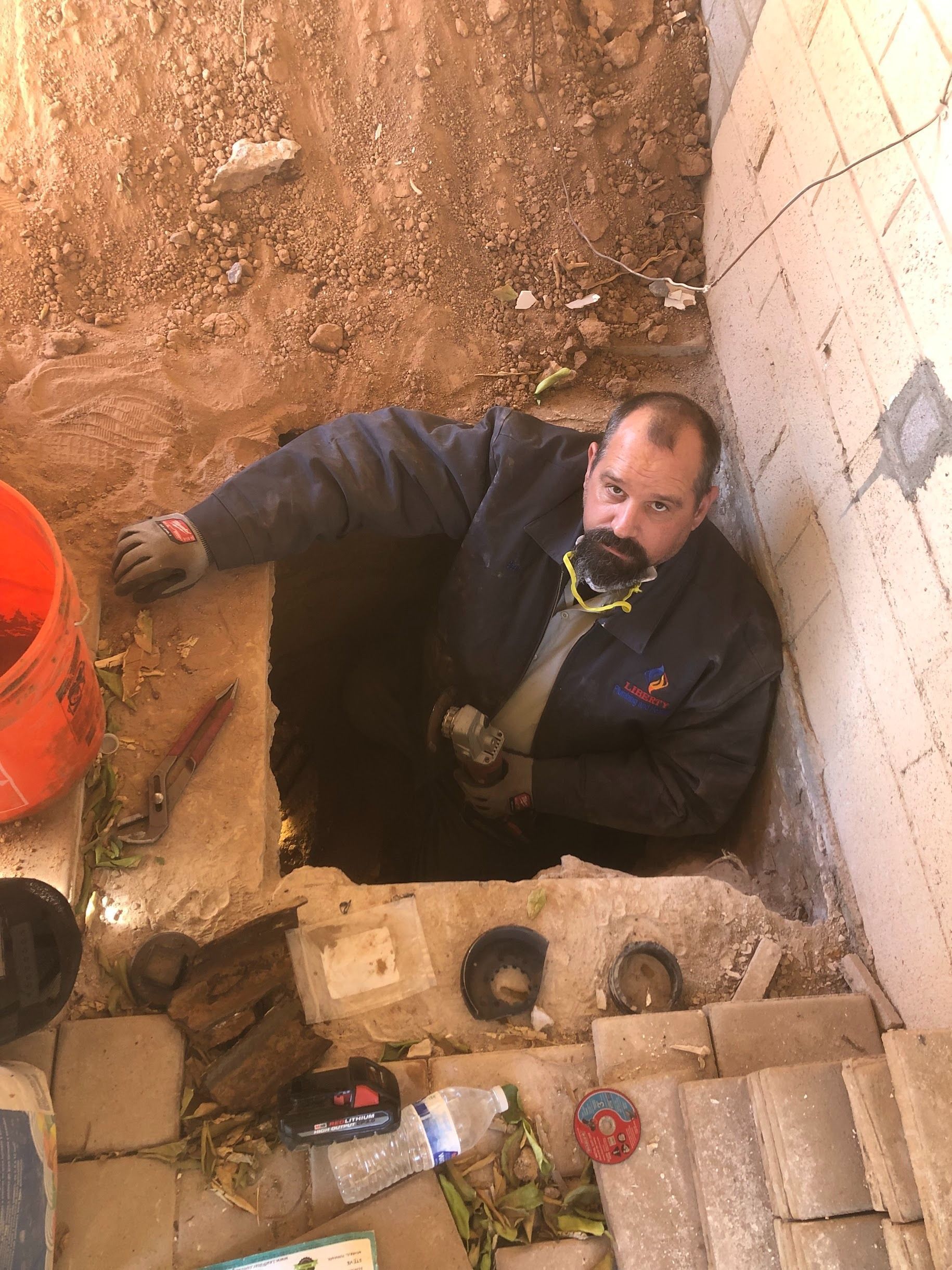 Man inside a hole, working. Surrounded by tools, dirt, and concrete.