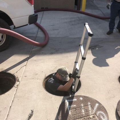 Man descending into a manhole with a ladder, red hose connected to a truck, on concrete.