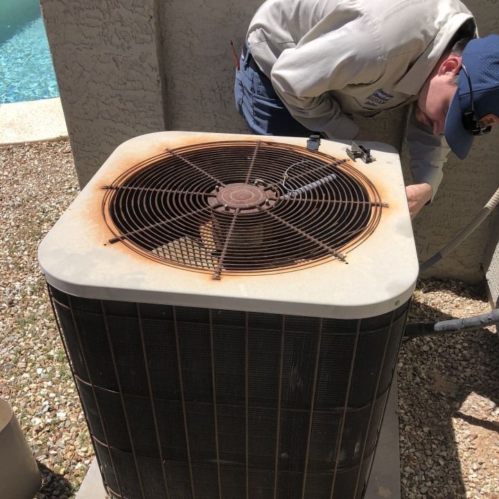 A technician inspects a rusty air conditioning unit next to a pool.