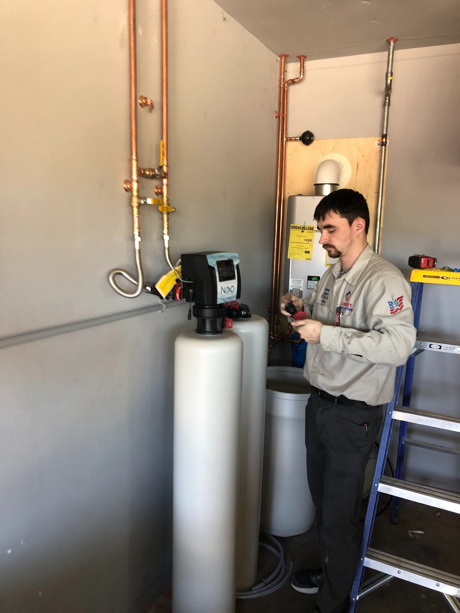 A technician working on a water softener system in a utility room with copper pipes.