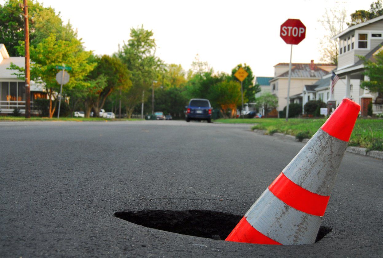 orange traffic cone inside a deep pothole located in the middle of a suburban road