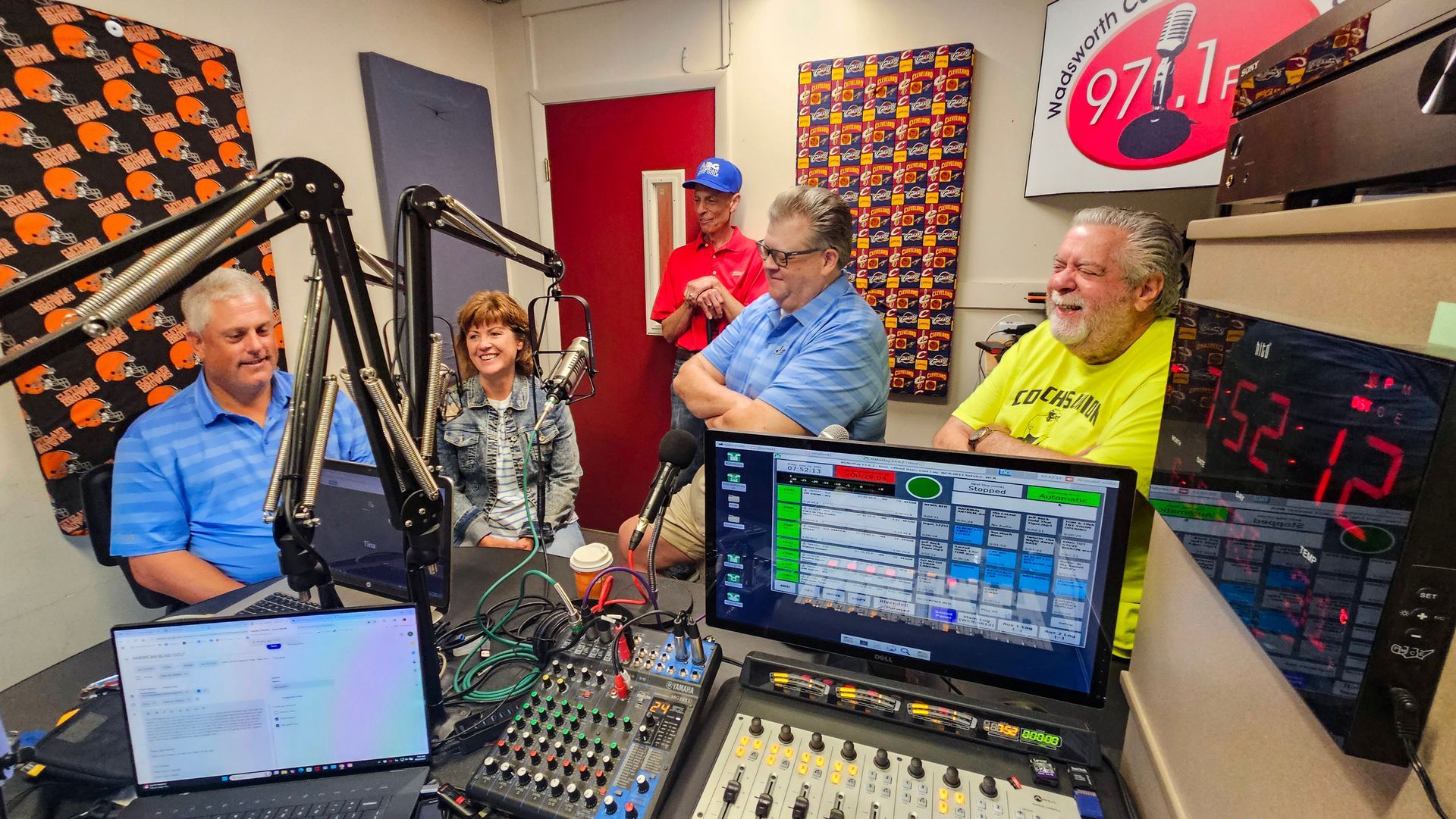 A group of people are sitting in front of a microphone in a radio studio.