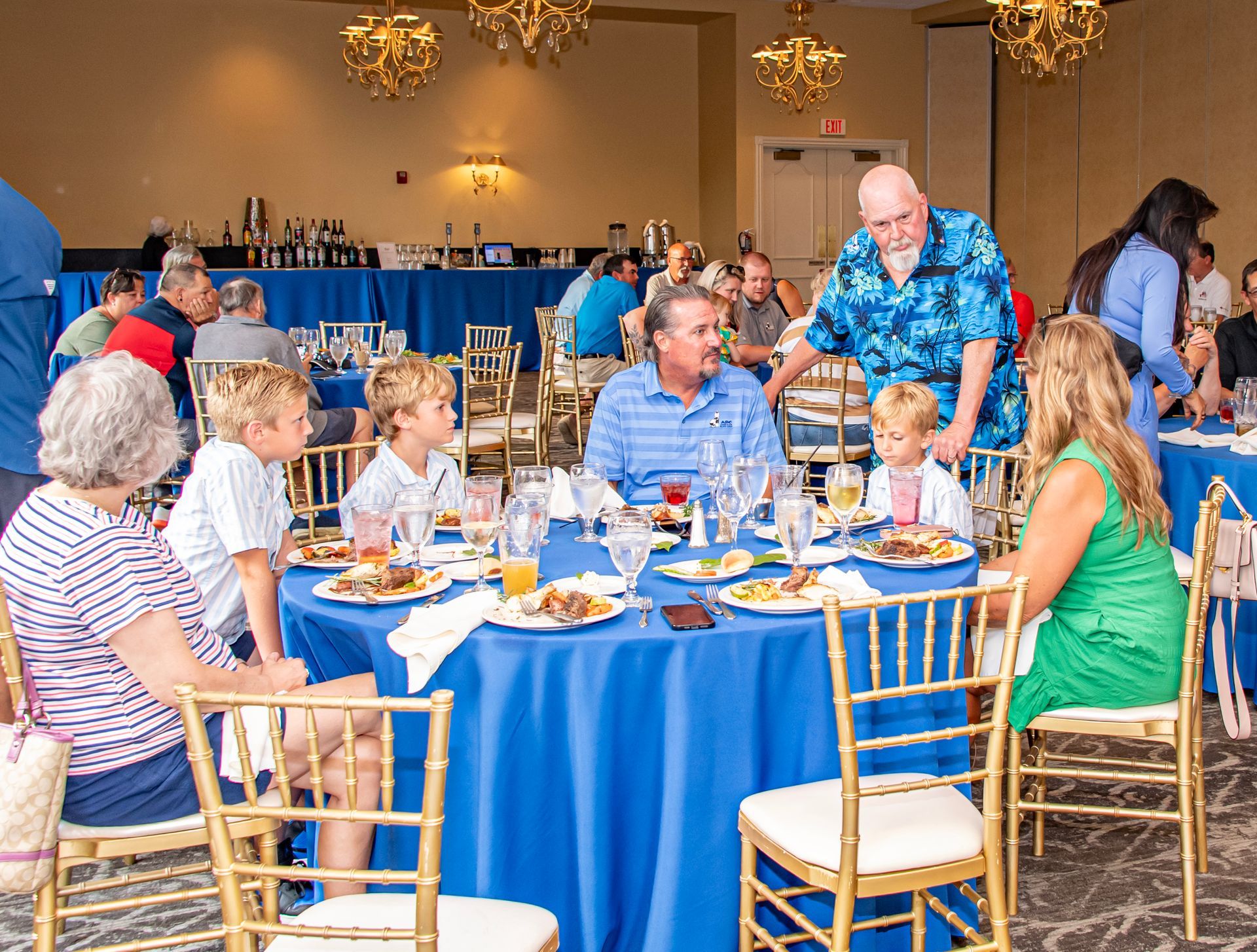 A group of people are sitting at tables with blue tables cloths.