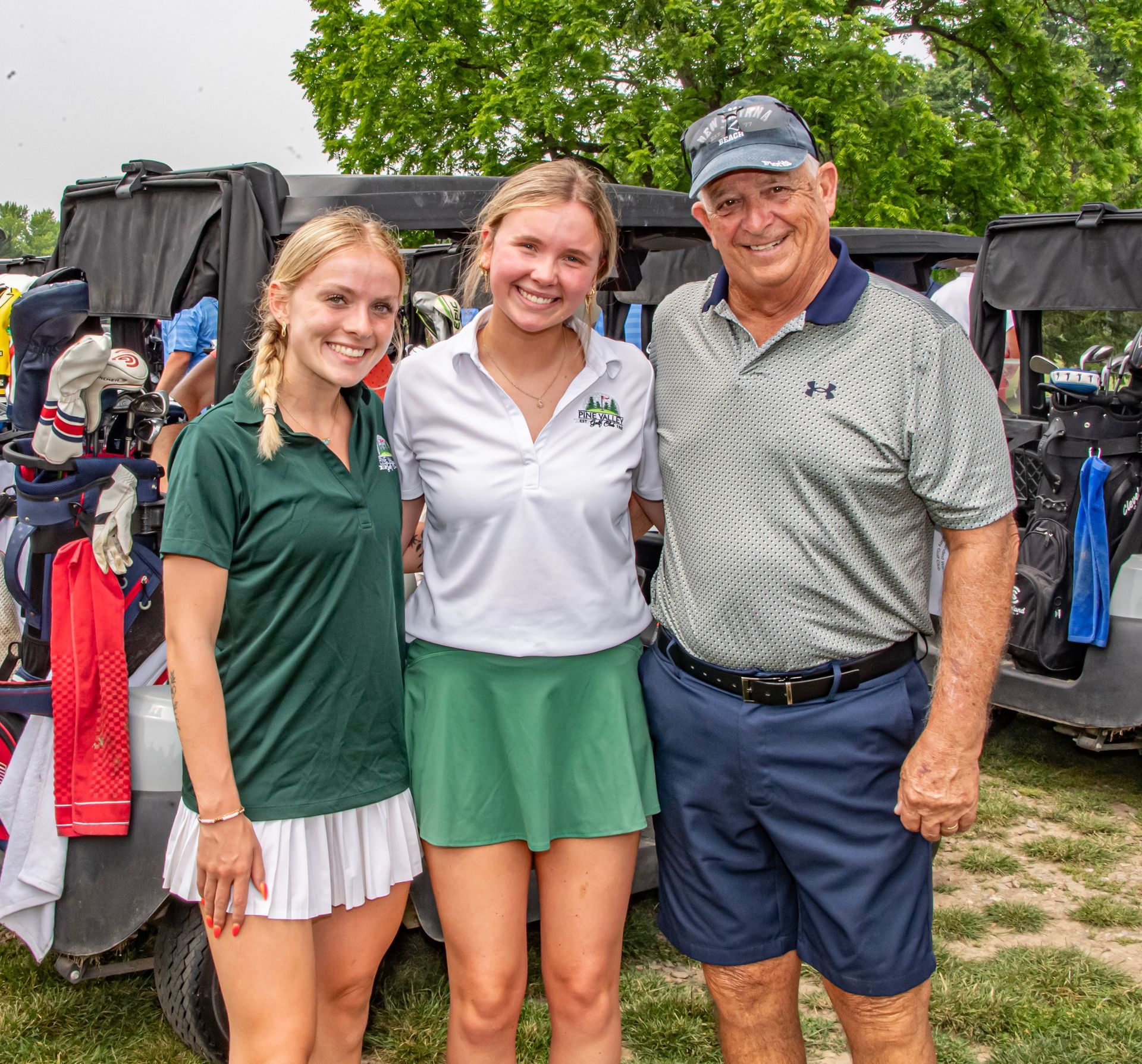 A man and two women are posing for a picture in front of a golf cart.