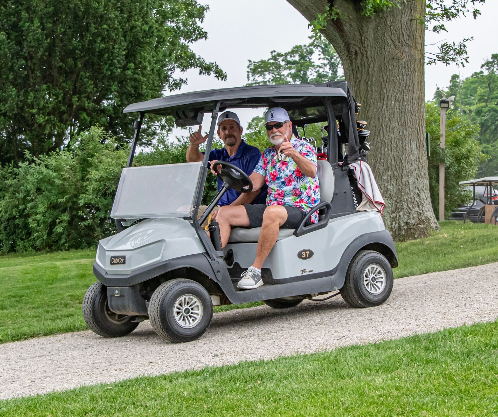 Two men are sitting in a golf cart on a gravel road.