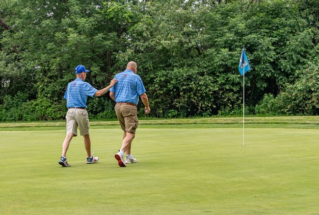 Two men are playing golf on a golf course in front of a house.