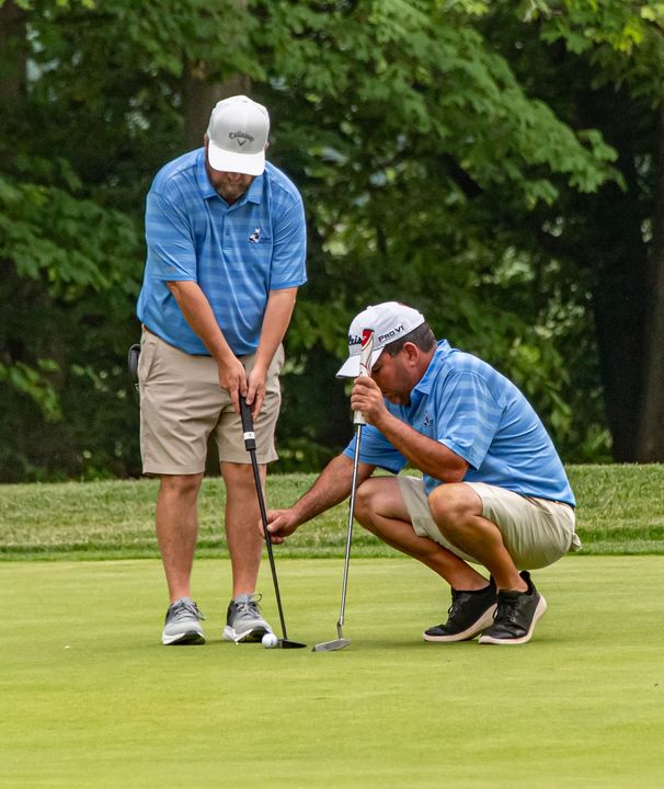 Two men are playing golf on a golf course in front of a house.