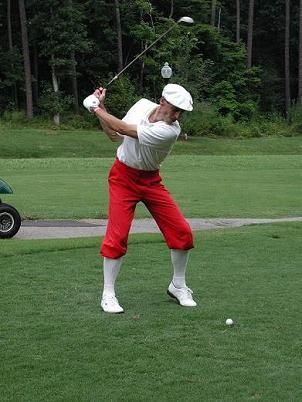 A man in red pants is swinging a golf club on a golf course.
