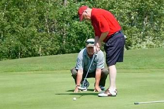 Denny McCulloch putting on a green while a man kneels to guide him