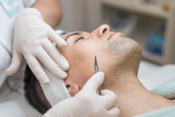 Man undergoing facial treatment with hands in gloves using a tool near his face.