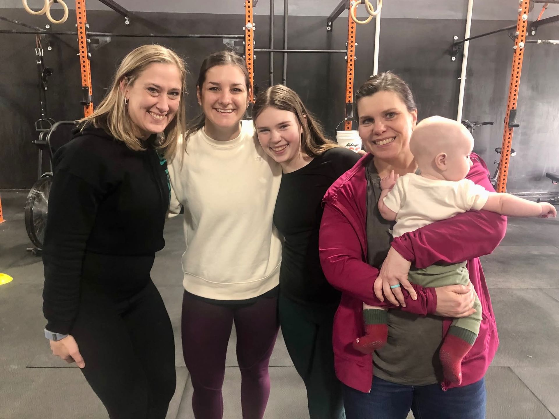 Five people, including a baby, pose in a gym setting.
