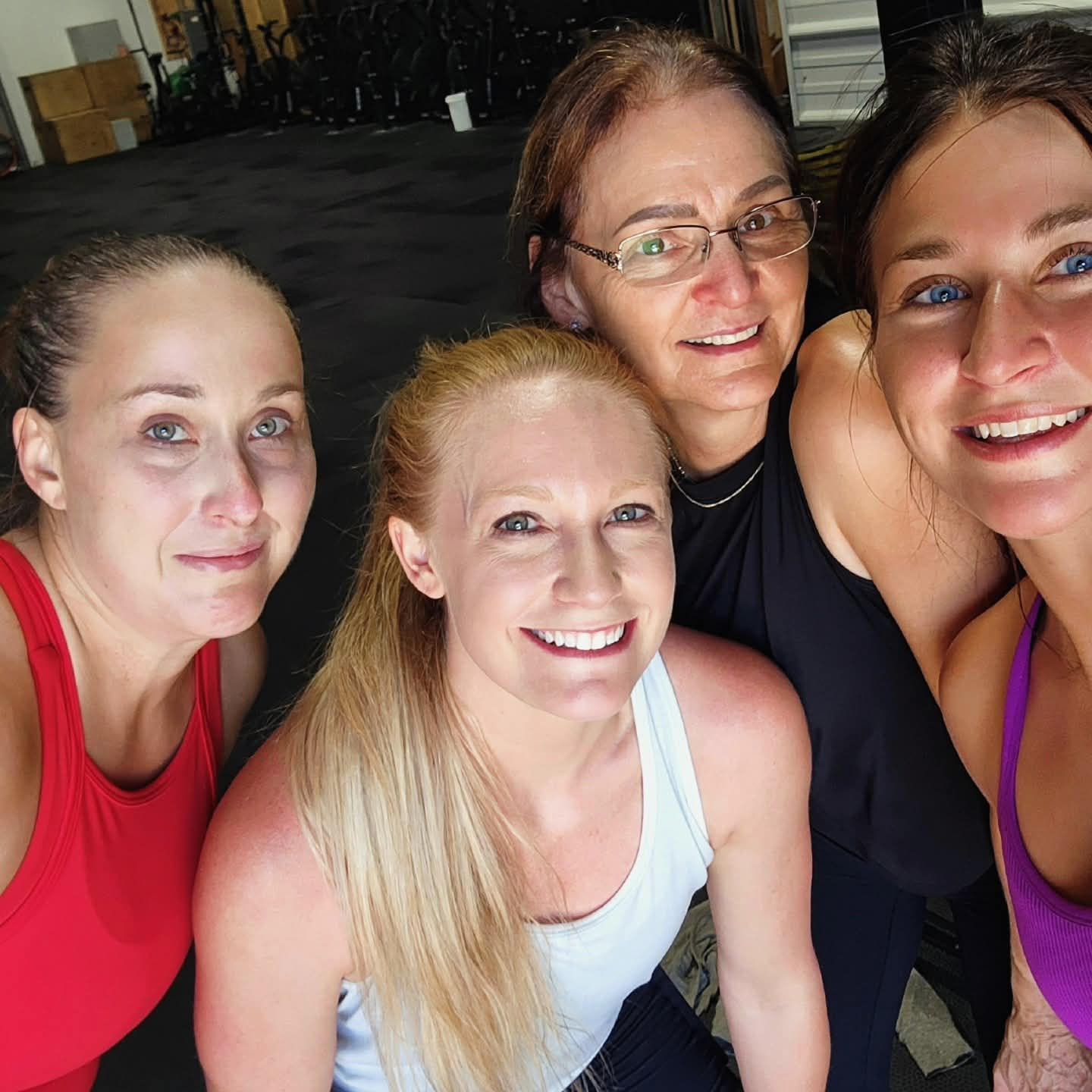 Four women smiling for a selfie indoors. They wear workout clothes.