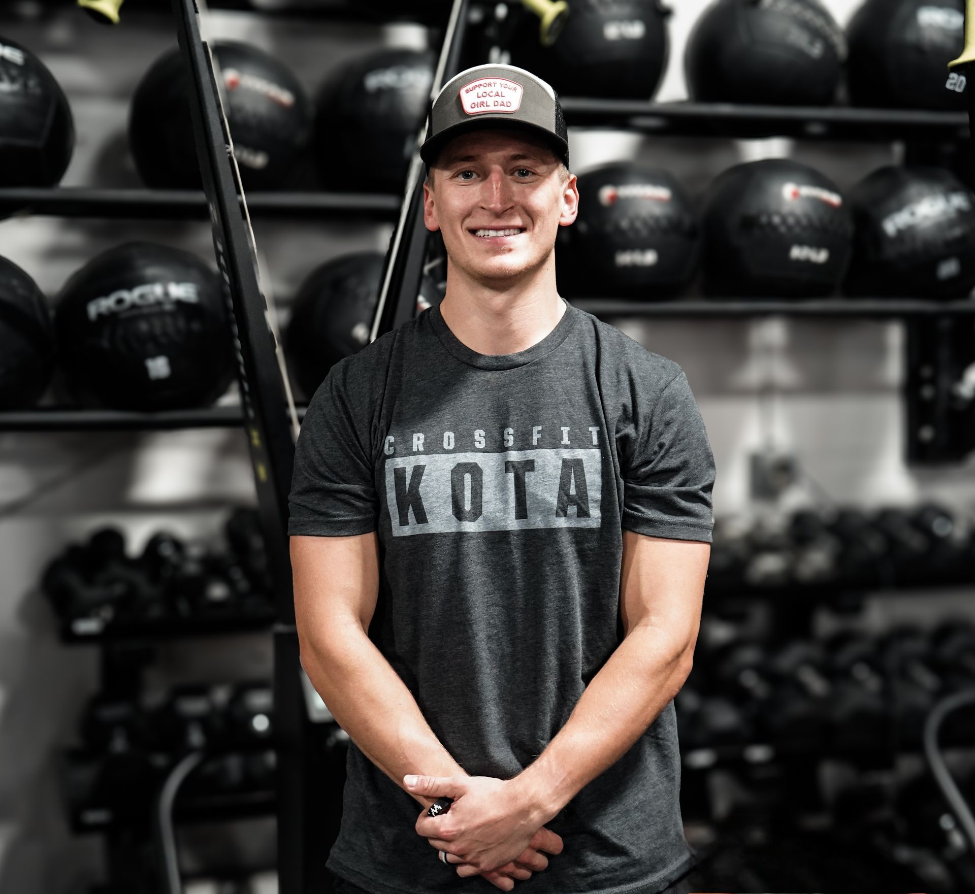 Man in CrossFit gym, smiling, wearing hat and grey shirt with