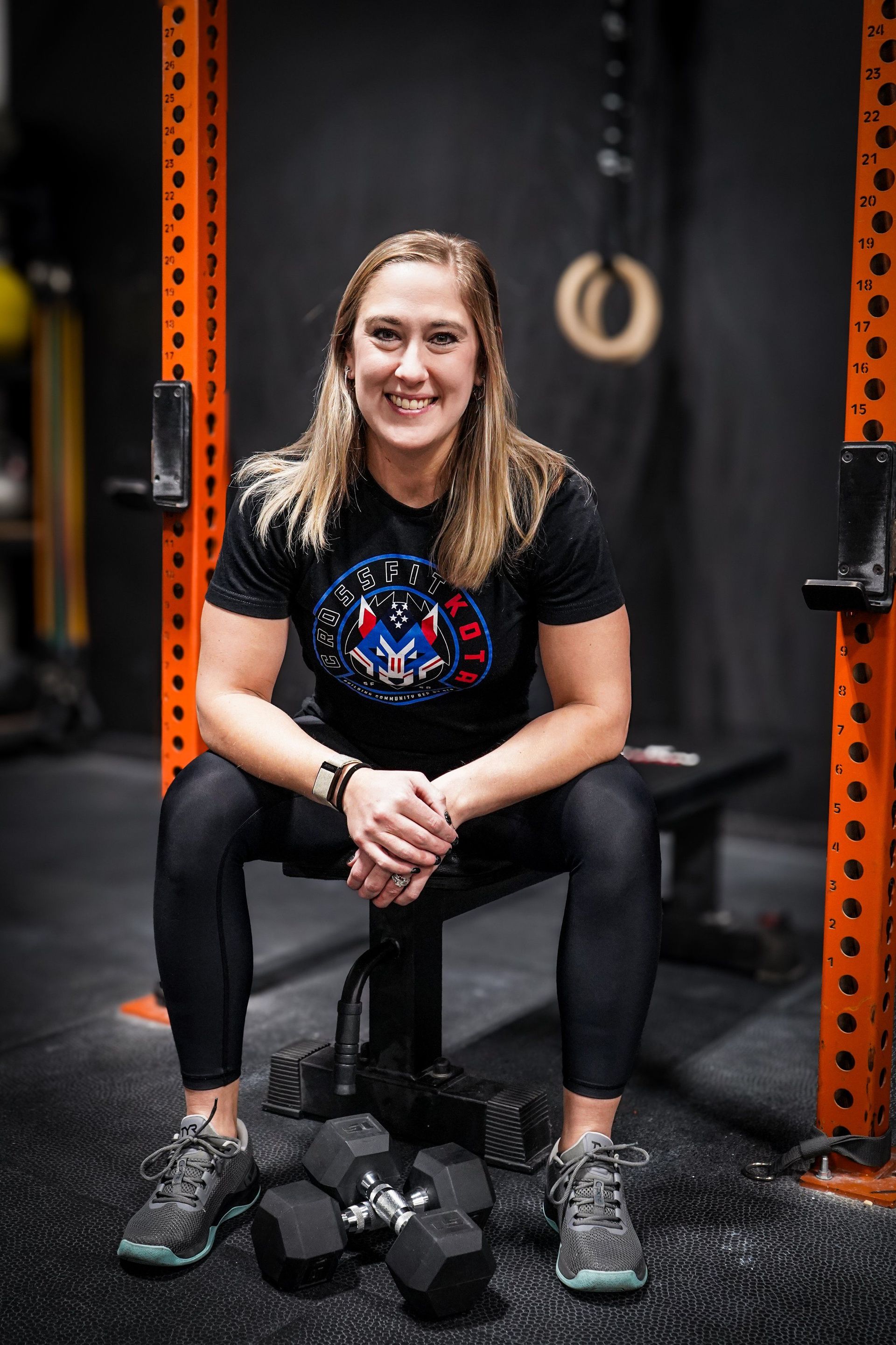 Woman in fitness attire sitting on bench, smiling, in gym setting.