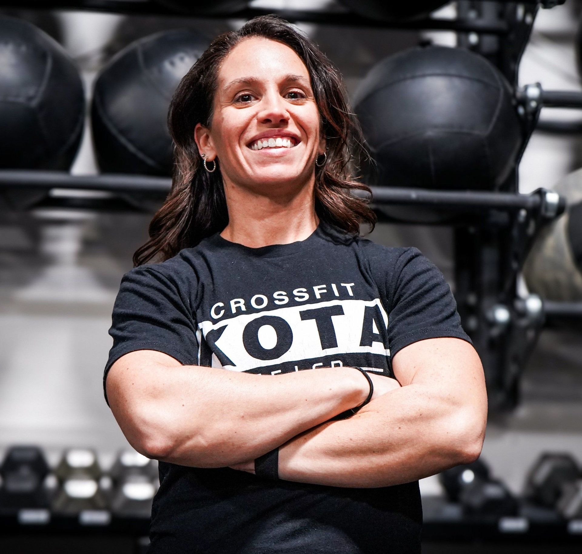 Woman with crossed arms in a CrossFit gym, smiling, wearing a
