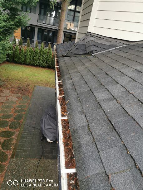 A gutter with leaves on it is on the roof of a house.