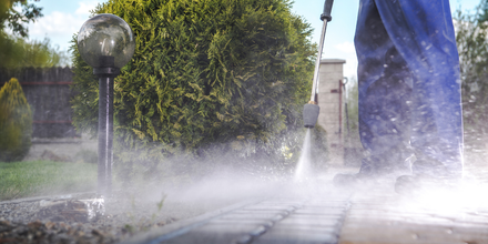 A man is using a high pressure washer to clean a sidewalk.