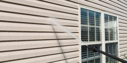 A person is cleaning the side of a house with a high pressure washer.
