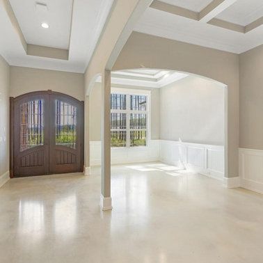 Interior of a new home with glossy light-colored floors, light walls, wooden double door, and arched doorway.