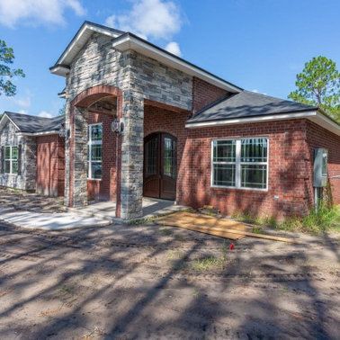 Brick house with stone accents, arched entryway, white-framed windows, construction site setting.