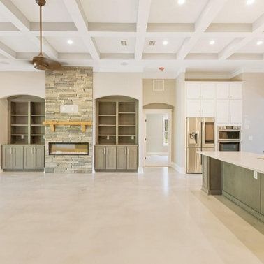Open-concept living space with fireplace, built-in shelving, kitchen, and light-colored flooring and walls.