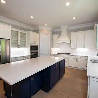 Spacious kitchen with white cabinets, navy island, stainless steel appliances, and light wood floors.