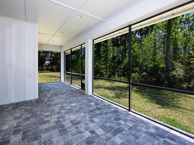 Screened porch with dark gray brick floor, overlooking a grassy yard and trees.