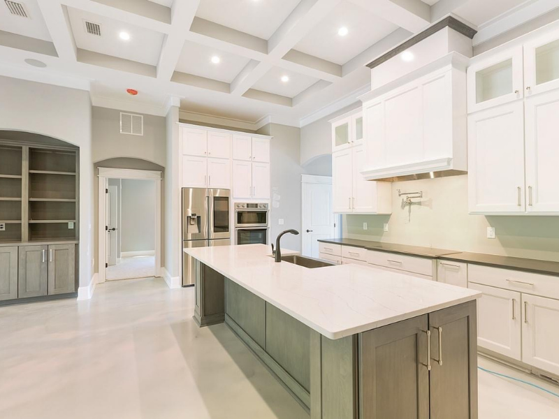 Modern kitchen with white cabinets, gray island, stainless steel appliances, and coffered ceiling.