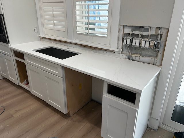 Kitchen countertop installation in progress; white cabinets, sink, and exposed wall with wiring.