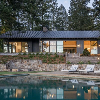 Modern home with dark siding, large windows, and a pool.