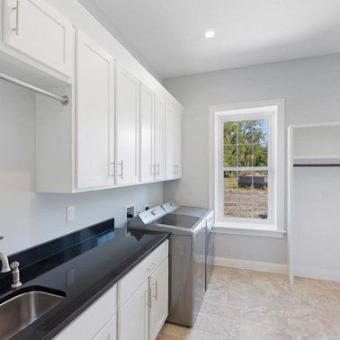 Laundry room with white cabinets, black countertop, stainless steel appliances, and a window.