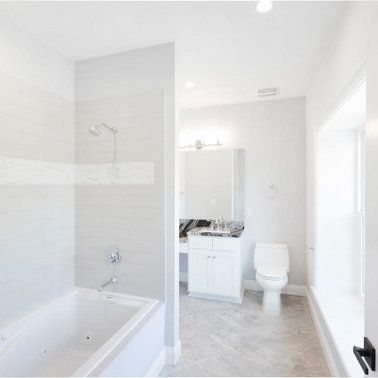 White bathroom with tub, shower, toilet, vanity, and window.