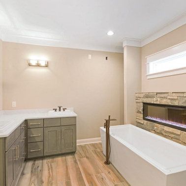 Bathroom with a tub, fireplace, cabinets, and light-colored walls and wood floor.