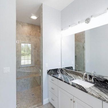 Bathroom with white cabinetry, black granite countertop, glass shower, and large mirror.