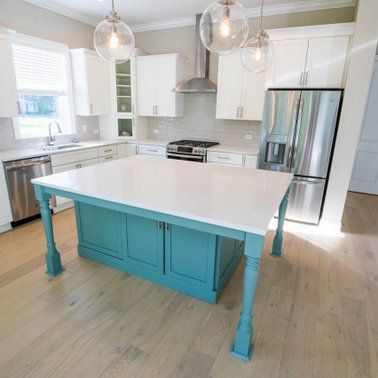 Bright kitchen with turquoise island, white cabinets, stainless steel appliances, and wood flooring.