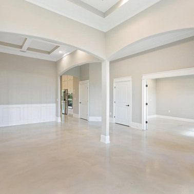 Empty, bright interior with arched doorways, white trim, and beige polished concrete floor.