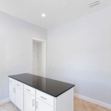 White kitchen island with a black countertop and white cabinets, in a room with light gray walls.