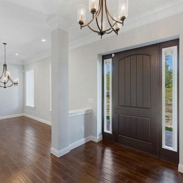 Entryway with dark brown door, hardwood floors, white walls, and chandeliers.