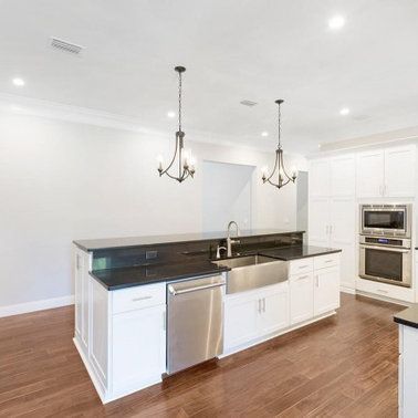 Modern white kitchen with island, stainless steel appliances, dark countertops, and pendant lights.