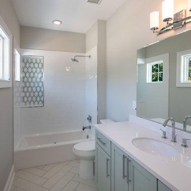 Light blue bathroom with a white sink, tub, and walls; tile accents and a large mirror.