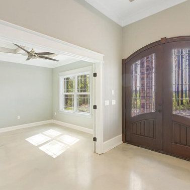 Interior view: entryway with brown double doors and an adjacent room with windows and a ceiling fan.