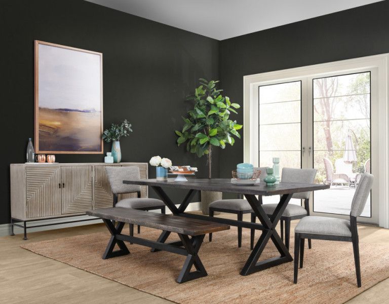 Dining room with dark walls, wooden table and bench, gray chairs, buffet, and large artwork.