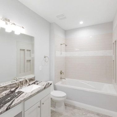 Bathroom with a white bathtub, toilet, vanity, and a light gray wall.