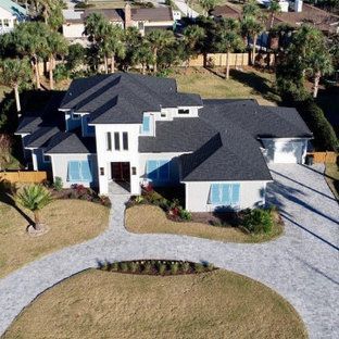 Aerial view of a large white house with a dark roof and circular driveway surrounded by palm trees.