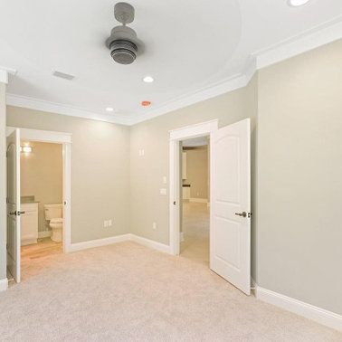 Empty room with beige walls, white trim, carpet, and three open doorways. Ceiling fan and recessed lights.