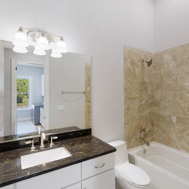 Bathroom with white vanity, dark countertop, and marble-look shower surround.
